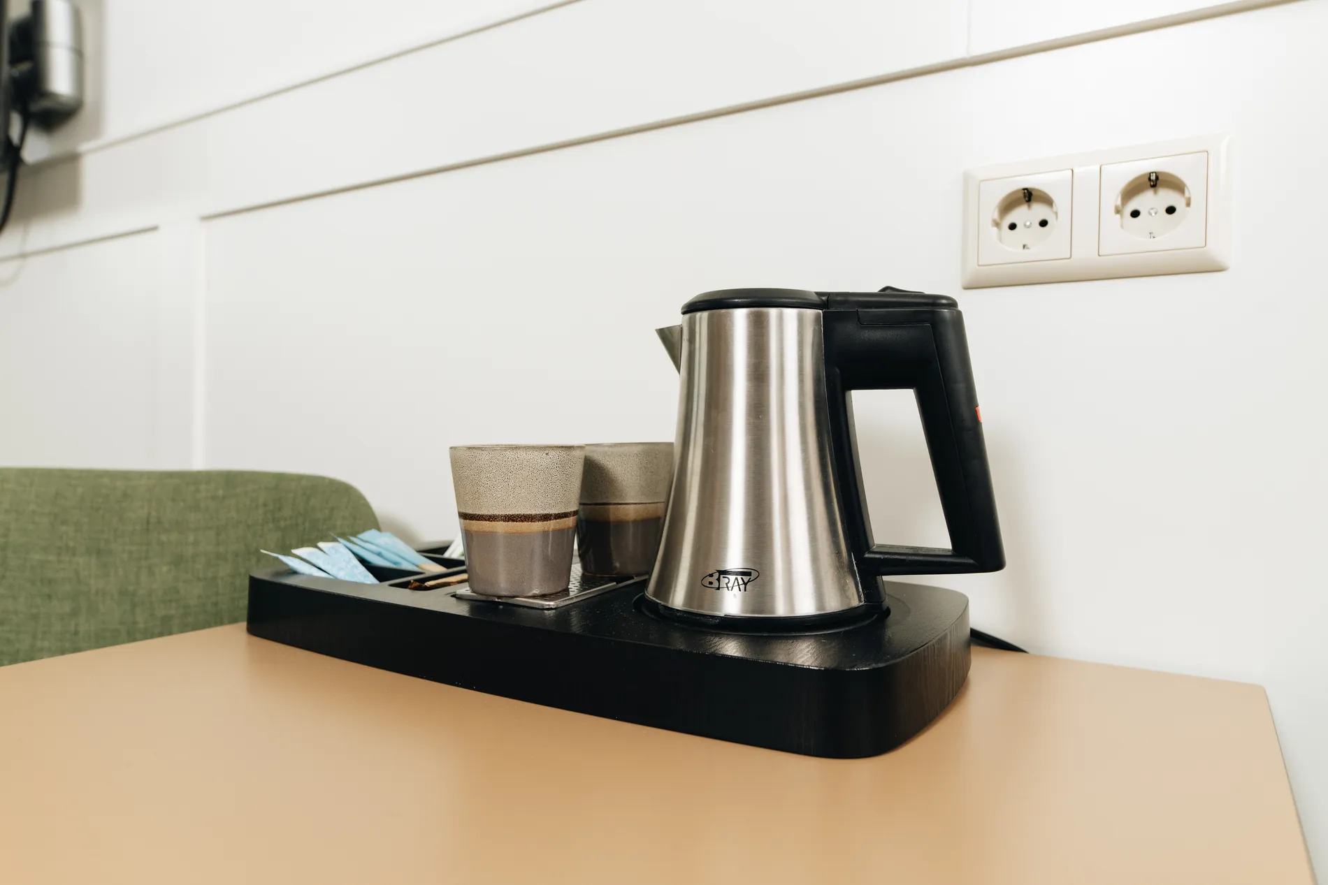 Koffie- en theefaciliteiten op de kamer, bestaande uit een roestvrijstalen waterkoker en luxe aardewerk bekers op een stijlvol zwart dienblad.